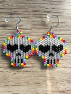 a pair of beaded earrings with a skull on it's face, sitting on a wooden surface