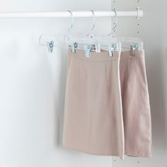 two pink skirts hanging on a white wall next to a coat rack with clothes hangers