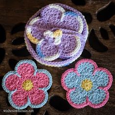 three crocheted flower coasters sitting on top of a wooden table next to each other