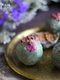 three chocolate covered donuts on a gold plate with purple and pink flowers in the background