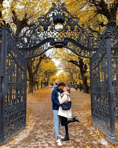 a man and woman standing under an iron gate in the fall with leaves on the ground