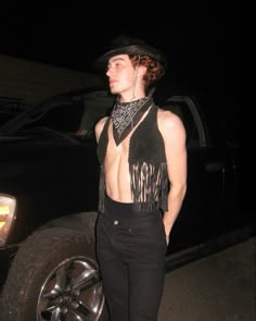 a young man wearing a hat and black outfit standing in front of a truck at night