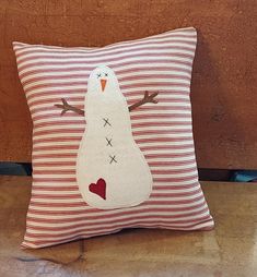 a red and white striped pillow with a snowman on the front, sitting on a wooden surface