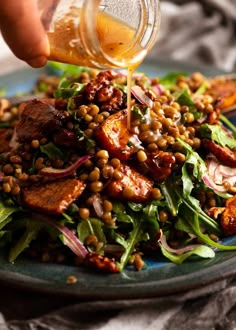 someone pouring dressing onto a salad on a blue plate with greens and lentulas