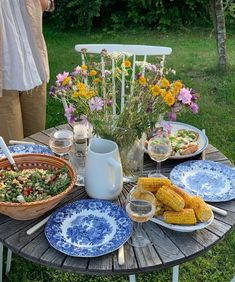 a table topped with plates and bowls filled with food next to corn on the cob