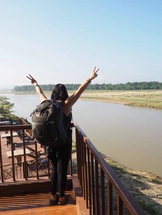 a woman with her arms outstretched on a balcony overlooking a river and grassy area in the distance