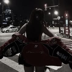 a woman with her back turned to the camera, walking across a street at night