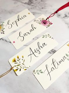 three name tags with flowers on them sitting on a marble counter top next to a red ribbon