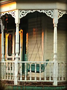 an old porch with a swing on the front and side of it, next to a house