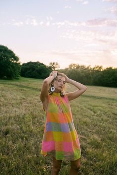 a woman standing in a field with her hands on her head wearing a colorful dress