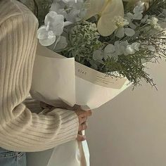 a woman holding a bouquet of flowers in her hands and wearing a sweater over her shoulders