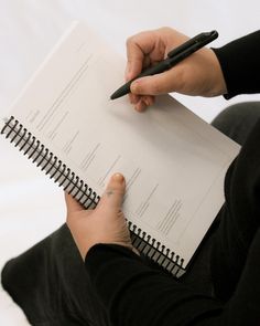 a person holding a pen and paper in their hand while sitting on the floor next to a notebook