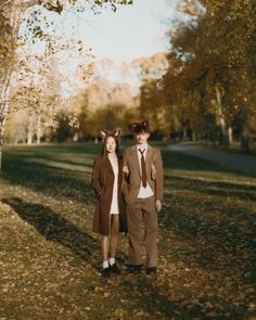 two people standing in the middle of a field with leaves on the ground and trees behind them