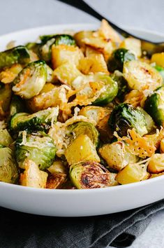 a white bowl filled with brussel sprouts and potatoes