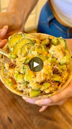 a person holding a bowl filled with food on top of a wooden table