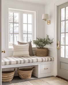 a window seat with pillows and baskets in front of the windows, next to a potted plant