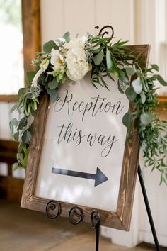 a sign that says reception this way with flowers and greenery on it, sitting in front of a window