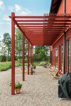 an outdoor covered patio area with chairs and potted plants on gravel ground next to red building