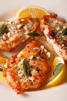 three pieces of chicken with herbs and lemon on a white plate