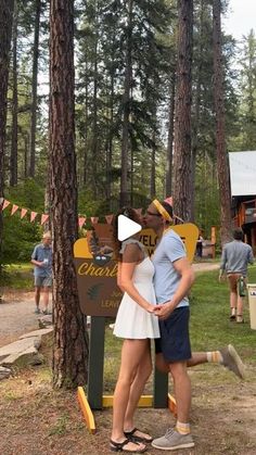 a man and woman standing next to each other in front of a sign with trees