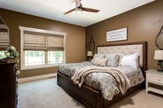 a bedroom with brown walls and carpeted flooring has a large bed, two nightstands, and a ceiling fan