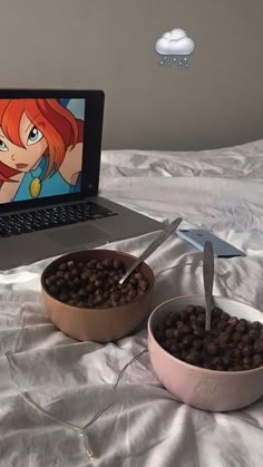 a laptop computer sitting on top of a bed next to two bowls filled with food