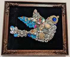 a wooden frame holding a brooch with many different colored stones and beads on it