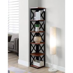 a tall shelf with books on top of it in a living room next to a lamp