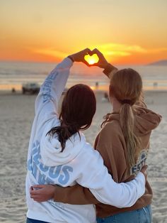 two girls making a heart shape with their hands on the beach at sunset or sunrise