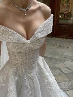 a woman wearing a wedding dress with an off the shoulder neckline and beading