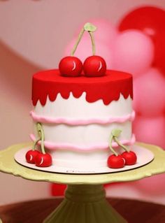 a red and white cake with cherries on top sitting on a table next to balloons