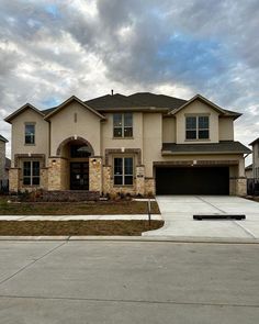 a large house with two garages and a driveway in front of it on a cloudy day