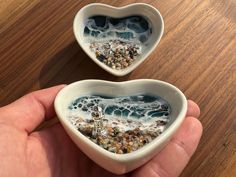 two heart shaped bowls filled with sand and sea shells