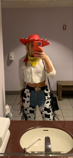 a woman taking a selfie in front of a mirror wearing cow print pants and a cowboy hat