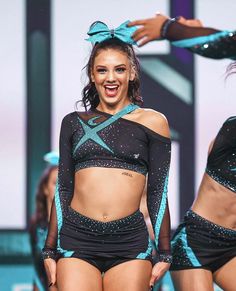 a woman in black and blue outfit standing on stage with other women behind her smiling at the camera