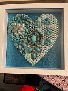 a heart made out of beads and other items in a white frame on top of a table