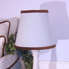 a white lamp sitting on top of a table next to a bed with pillows and blankets