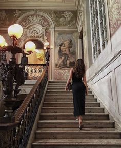 a woman is walking down the stairs in an old building with paintings on the walls