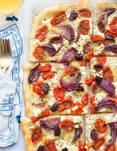 a square pizza with onions, cheese and tomatoes on it next to a fork and knife