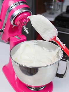 a mixer filled with white icing next to a pink hand mixer on top of a counter