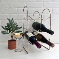 three wine bottles and two glasses on a stand next to a potted plant, with a brick wall in the background