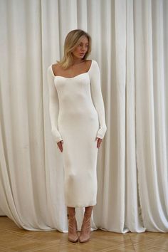 a woman standing in front of a curtain wearing a white sweater dress and high heels