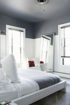 a white bed sitting in a bedroom next to two windows