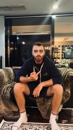 a man sitting on top of a couch in front of a glass door with his fingers crossed