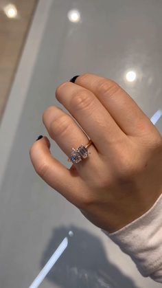 a woman's hand with a diamond ring on top of her finger, in front of a glass display case