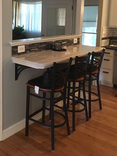 a kitchen counter with four stools and a sink in the middle, along with a mirror on the wall