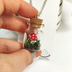 a hand holding a tiny glass jar with moss and mushrooms in it on a chain