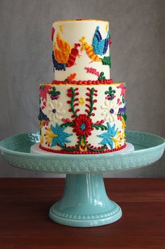 a multi - tiered cake decorated with birds and flowers on a blue plate, sitting on a wooden table