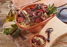 a wooden cutting board topped with a bowl filled with meat and rice next to a bottle of olive oil