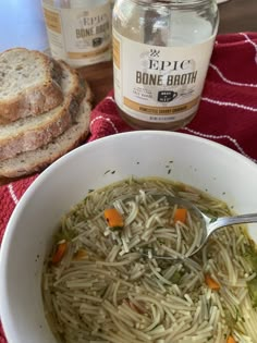 a bowl of soup with noodles and carrots next to some bread on a table